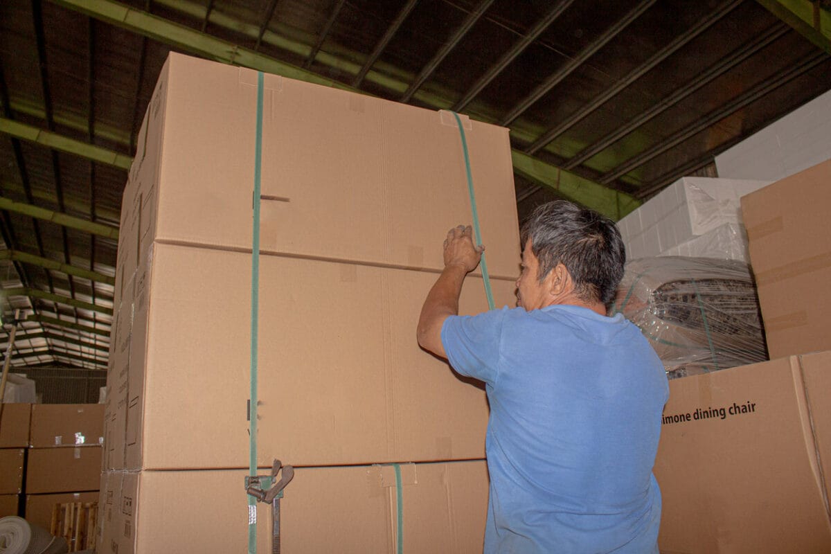 Furniture export logistics in Vietnam showing a worker securing packaged furniture cartons with straps