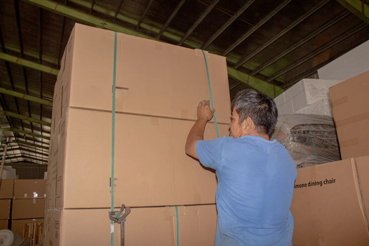 Furniture export logistics in Vietnam showing a worker securing packaged furniture cartons with straps