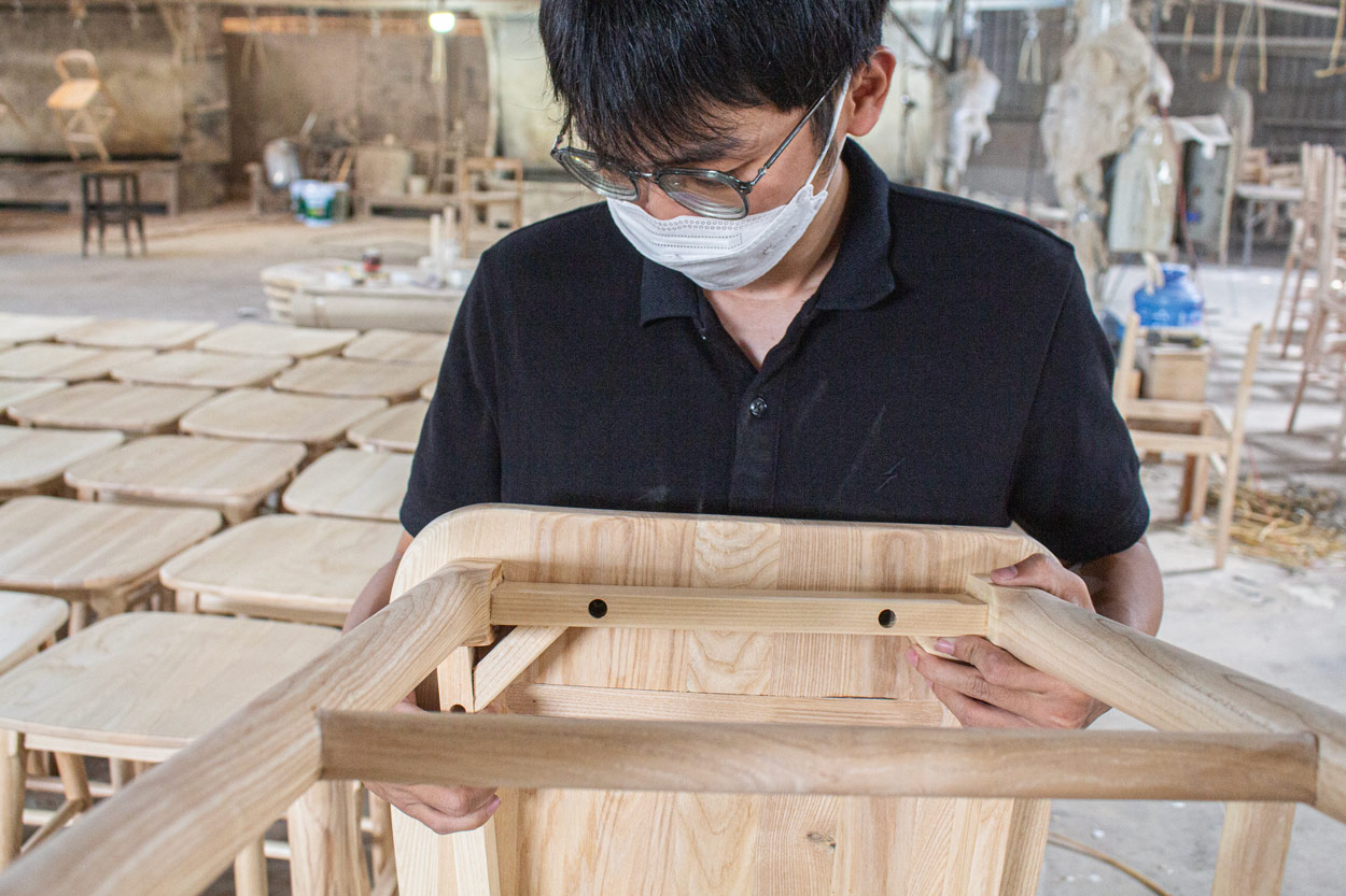 Worker visually inspecting the wooden frame and construction of a furniture product during quality control